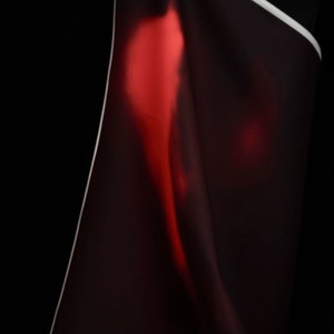 May include: A close-up of a dark red fabric with a subtle sheen. The fabric is draped and folded, creating a soft, abstract pattern.