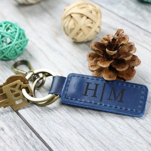 May include: A blue leather keyring with a gold metal key ring and two keys. The keyring has the initials "H|M" engraved in black.