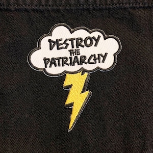 May include: A white cloud with the text "Destroy the Patriarchy" in black lettering, with a yellow lightning bolt underneath. The patch is on a black fabric background.