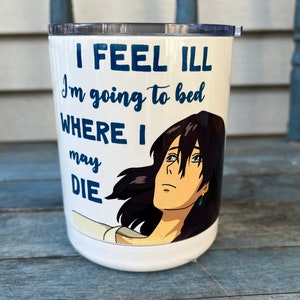 May include: White travel mug with a blue and white graphic of a woman with long black hair and the text "I feel ill I'm going to bed where I may die".