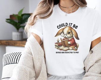 May include: White t-shirt with a graphic of a bunny wearing glasses and reading a book. The text on the shirt reads "Could it be books are addicted to me?"