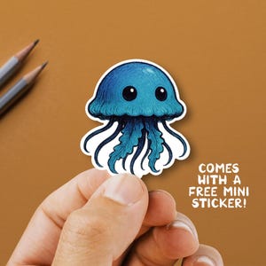 May include: A blue jellyfish sticker with a detailed illustration. The sticker has a white border and the text "COMES WITH A FREE MINI STICKER!" on a brown background. The jellyfish has large black eyes.