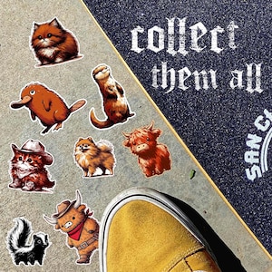 May include: A collection of animal stickers, including a cat, a platypus, a skunk, and a highland cow, are displayed on a concrete surface next to a skateboard. The skateboard has the text "collect them all" in white lettering. A yellow shoe is in the foreground.