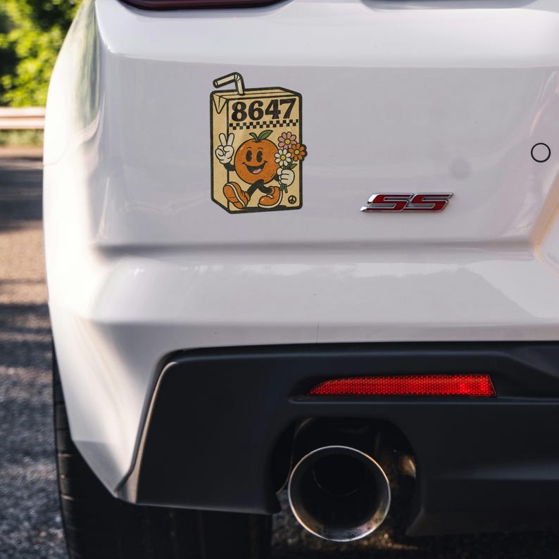 May include: A retro-style sticker featuring a smiling orange character in a juice box. The character is giving a peace sign and holding flowers. The juice box has the number "8647" printed on it. The sticker is affixed to the rear of a white car.