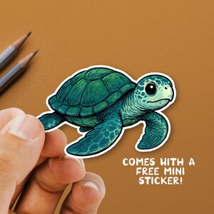 May include: A green sea turtle sticker with a white border. The turtle has a detailed shell and flippers. The text "COMES WITH A FREE MINI STICKER!" is printed in white.