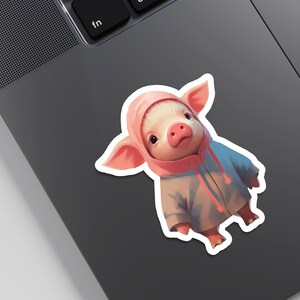 May include: A pink pig wearing a pink and blue hooded jacket. The pig is looking at the camera with a curious expression.