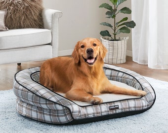 Peut inclure: Un lit pour chien en plaid brun et blanc avec une bordure noire. Le lit a un bord surélevé et une doublure douce et moelleuse. Un chien golden retriever est allongé sur le lit, regardant la caméra et souriant. Le lit porte le logo Kirkland Signature sur le côté.