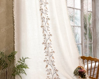 May include: An off-white curtain panel featuring a vertical embroidered vine pattern in light brown. The fabric has a textured weave and is finished with small, dangling tassels along the side and bottom edges, creating a decorative border.