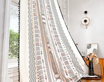 May include: Cream-colored curtain with a geometric pattern in black, gray, and rust. The curtain features a zigzag and linear design, with black tassels along the edges. The curtain is hanging in front of a window.