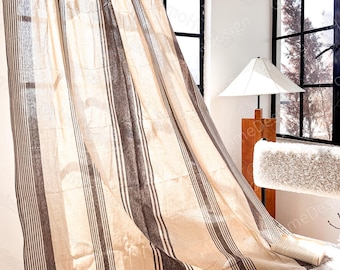 May include: A semi-sheer curtain panel featuring a pattern of wide and narrow vertical stripes in dark brown and beige. The fabric has a textured appearance and hangs in soft folds, allowing light to filter through the weave of the material.