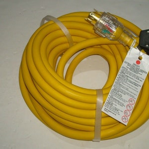 Peut inclure: Un cordon d'extension robuste de 15 mètres de couleur jaune avec une prise et une fiche à 3 broches. Le cordon est enroulé et une étiquette d'avertissement est fixée.