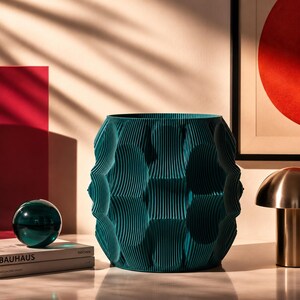 Può includere: Un vaso cilindrico color verde acqua caratterizzato da una texture a coste verticali ripetute con una serie di rientranze concave lungo l'esterno. L'oggetto presenta un'ampia apertura superiore e una base solida di colore blu-verde intenso.