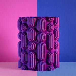 May include: A cylindrical, purple vase with a textured, layered design. The vase features a pattern of rounded, vertical shapes and spheres. The background is split between pink and blue.