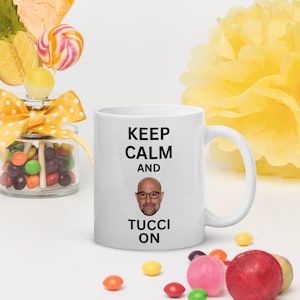 Puede incluir: Taza de cerámica blanca con texto negro que dice "Keep Calm and Tucci On". Una foto en blanco y negro del actor Stanley Tucci está en el centro de la taza.