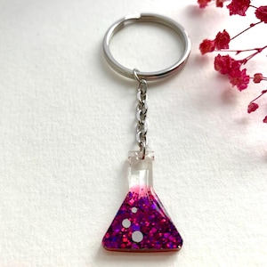 Op de afbeelding: Een zilveren sleutelhanger met een glazen bekerbedel gevuld met roze en paarse glitter.