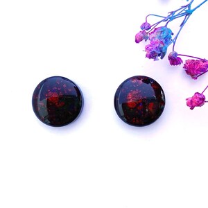May include: A pair of round, black resin earrings with red and blue glitter embedded in the resin.