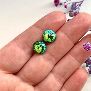 May include: A pair of green and yellow round stud earrings with a speckled pattern.