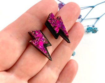 May include: A pair of black lightning bolt shaped earrings with pink glitter embedded in the resin.