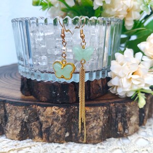 May include: A pair of gold butterfly earrings with green butterfly charms. One earring has a gold tassel.