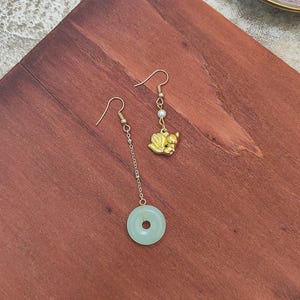 May include: A pair of gold earrings with a jade pendant and a gold animal charm. The jade pendant is a light green colour and the animal charm is a gold squirrel.