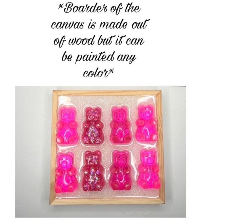 Op de afbeelding: Een houten frame met een witte achtergrond bevat acht roze gummybeer-vormige hars sculpturen. De gummyberen hebben glitter ingebed. De tekst "*Boarder of the canvas is made out of wood but it can be painted any color*" staat boven het frame.