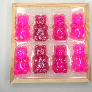Op de afbeelding: Een houten frame met een transparante achtergrond en acht roze gummybeertjes. De gummybeertjes zijn gerangschikt in twee rijen van vier. Sommige van de gummybeertjes hebben glitter erin verwerkt.