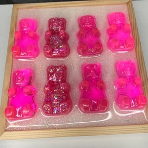 Op de afbeelding: Negen roze gummybeertjes in de vorm van beren met glitter erin verwerkt. De gummybeertjes zijn gerangschikt in een raster op een witte achtergrond met glitter.