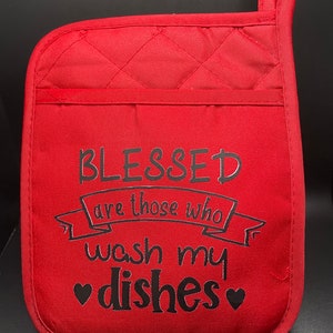 May include: Red quilted oven mitt with a black embroidered saying "Blessed are those who wash my dishes" with hearts around the word dishes.