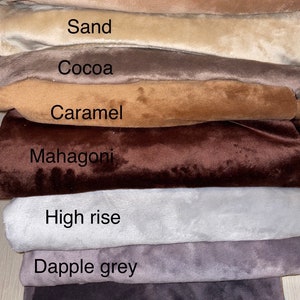 May include: A stack of eight fabric swatches in different shades of brown, gray, and beige. The swatches are labeled with the following names: Simple Taupe, Sand, Cocoa, Caramel, Mahogany, High Rise, Dapple Grey, and Pewter.