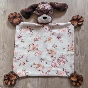 May include: A brown and white puppy-shaped security blanket with a floral pattern and the name "Love" embroidered on it.