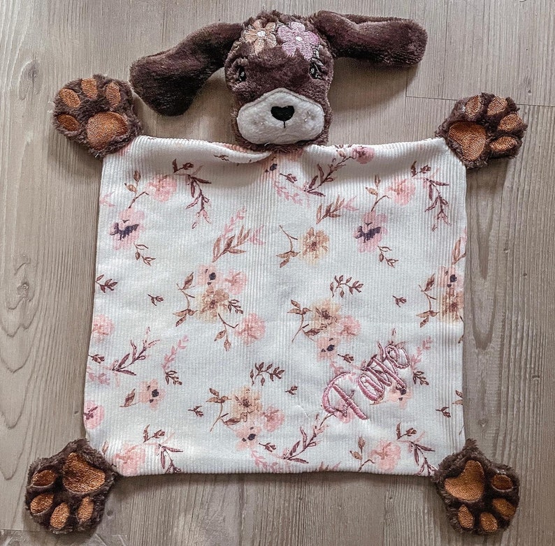 May include: A brown and white puppy-shaped security blanket with a floral pattern and the name "Love" embroidered on it.
