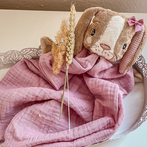 May include: A plush brown and white bunny with a pink bow sits on a pink muslin blanket in a decorative metal tray. A dried wheat stalk is placed next to the bunny.
