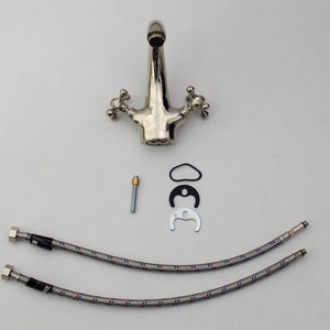 Pode incluir: Uma torneira de banheiro cromada com duas al&ccedil;as e um bico. A torneira &eacute; acompanhada por duas mangueiras tran&ccedil;adas, um pino de metal, uma arruela de borracha e um anel de metal.