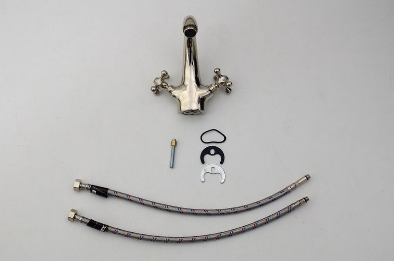 Pode incluir: Uma torneira de banheiro cromada com duas al&ccedil;as e um bico. A torneira &eacute; acompanhada por duas mangueiras tran&ccedil;adas, um pino de metal, uma arruela de borracha e um anel de metal.