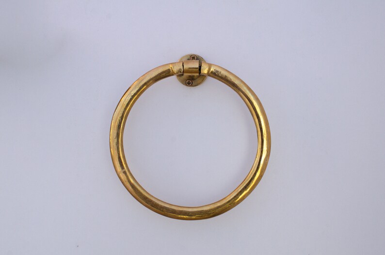 Puede incluir: Un anillo para toallas de metal dorado montado en una pared blanca.