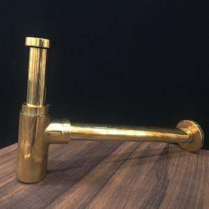 以下が含まれることがあります： 曲線的なデザインの金色の金属製排水管。管は光沢のある金属製で、滑らかな仕上げです。