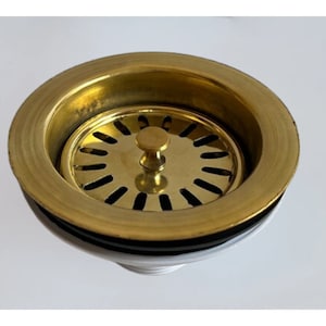 Può includere: Uno scolapiatti dorato con una parte superiore rotonda perforata e un piccolo pomello rotondo al centro.