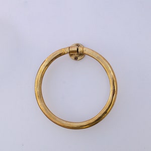 Puede incluir: Un anillo para toallas de metal dorado montado en una pared blanca.