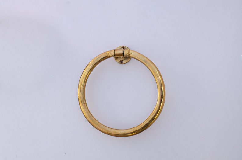 Puede incluir: Un anillo para toallas de metal dorado montado en una pared blanca.