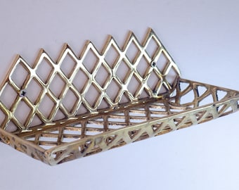May include: A gold metal wall shelf with a geometric diamond pattern. The shelf is made of a thin, open-weave metal and has a rectangular shape.