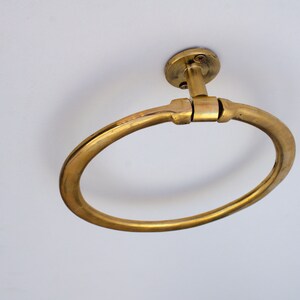 Puede incluir: Un anillo para toallas de metal dorado montado en un techo blanco. El anillo es circular y tiene un acabado liso y pulido.