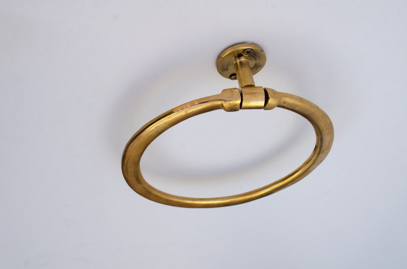 Puede incluir: Un anillo para toallas de metal dorado montado en un techo blanco. El anillo es circular y tiene un acabado liso y pulido.