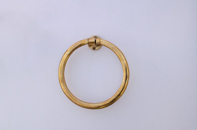 Puede incluir: Un anillo para toallas de metal dorado montado en una pared blanca.