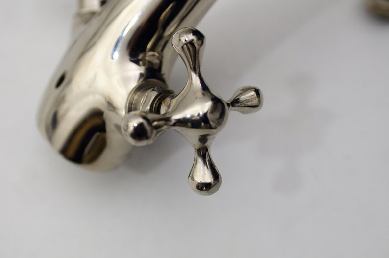 Pode incluir: Close-up de uma pega de torneira cromada com um design em forma de cruz. A pega &eacute; brilhante e reflete a luz.