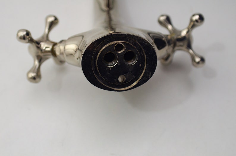 Pode incluir: Close-up de uma torneira cromada com duas al&ccedil;as em forma de cruz. A torneira tem tr&ecirc;s furos no bico, um grande e dois menores.