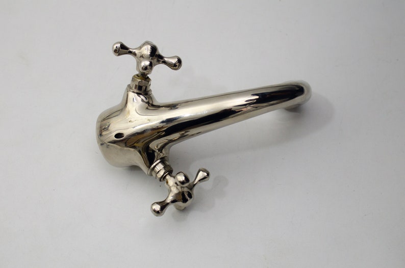 Pode incluir: Uma torneira cromada polida com duas al&ccedil;as em forma de cruz. A torneira tem um bico curvo e &eacute; projetada para uma pia de banheiro.