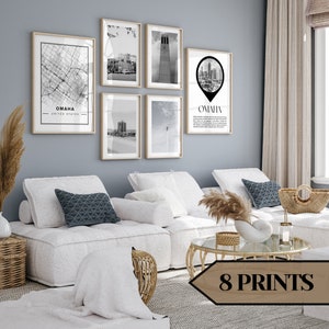 Puede incluir: Ocho impresiones en blanco y negro de Omaha, Nebraska, que se muestran en una pared sobre un sofá blanco con almohadas y una mesa de café. Las impresiones presentan un mapa, un horizonte y un edificio.