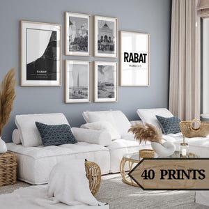Può includere: Un interno di soggiorno con un divano componibile bianco, un tavolino da caffè e un set di stampe incorniciate in bianco e nero sul muro. Le stampe presentano immagini di edifici e paesaggi urbani. Il testo "RABAT MOROCCO" è visibile su una delle stampe.