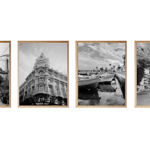 Può includere: Un set di quattro fotografie in bianco e nero incorniciate che ritraggono varie scene dall'Italia. La prima foto mostra una strada stretta fiancheggiata da edifici bianchi. La seconda foto mostra un edificio con un tetto a cupola. La terza foto mostra un porto con barche attraccate al molo. La quarta foto mostra una strada con edifici bianchi e tetti conici.