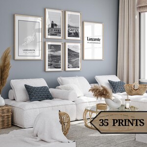 Puede incluir: Un interior de sala de estar con un sofá seccional blanco y una mesa de café de vidrio. La pared detrás del sofá está pintada de un color azul claro y presenta una pared de galería de fotografías en blanco y negro con el texto "Lanzarote Islas Canarias".